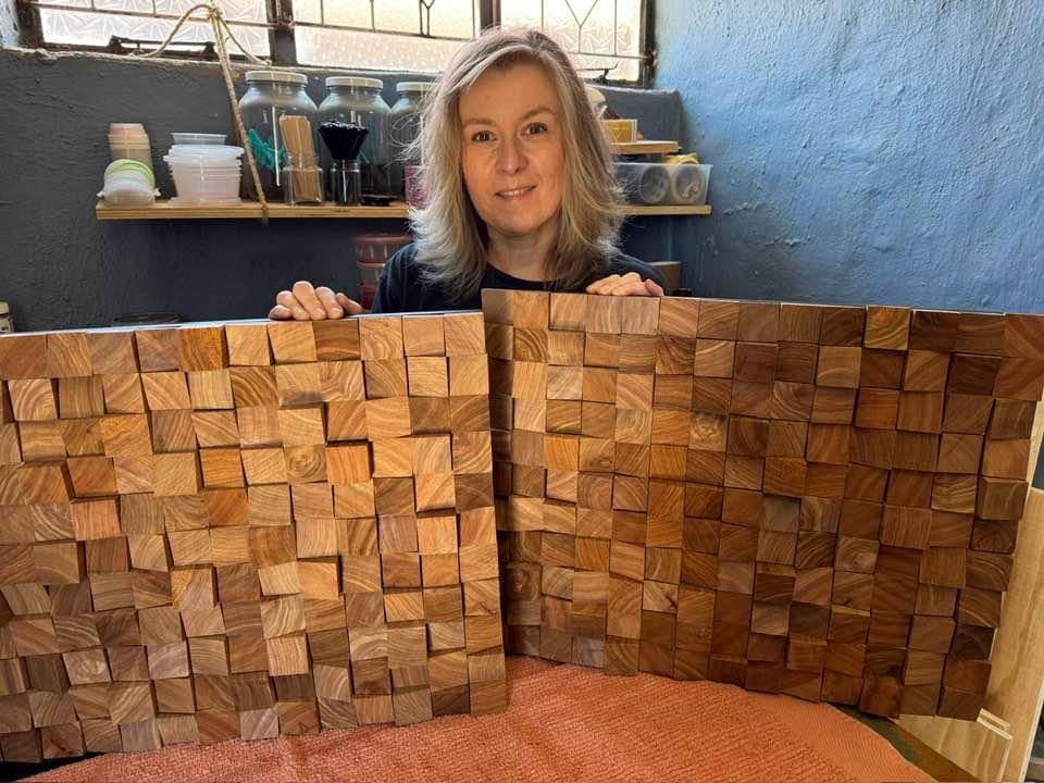 Handmade wood wall art panels crafted from rich Kiaat wood, held by the artist in her Johannesburg studio. The pieces showcase bold texture and grain variation.