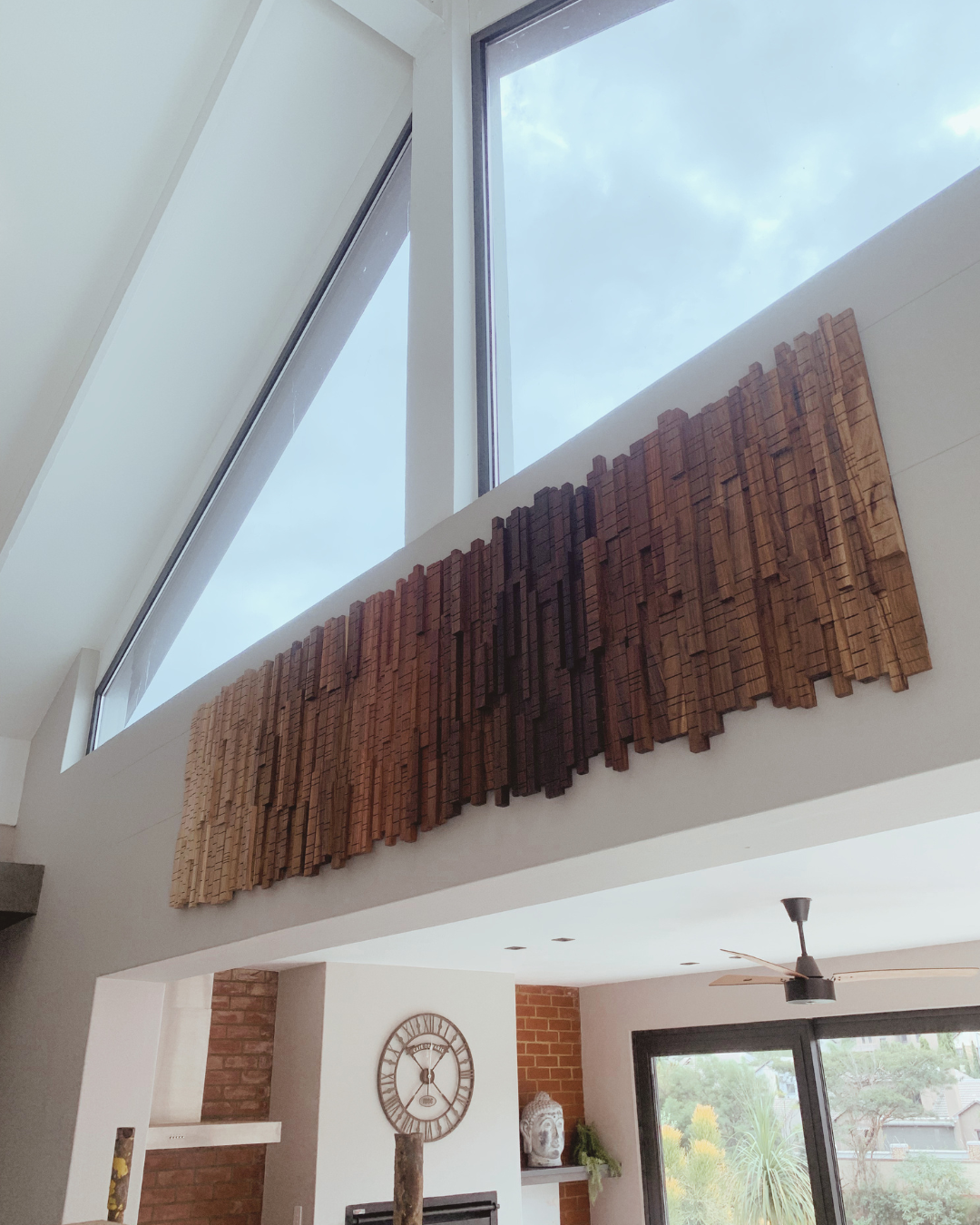 Large bespoke wooden wall art installed beneath dramatic triangular windows in a contemporary South African home.