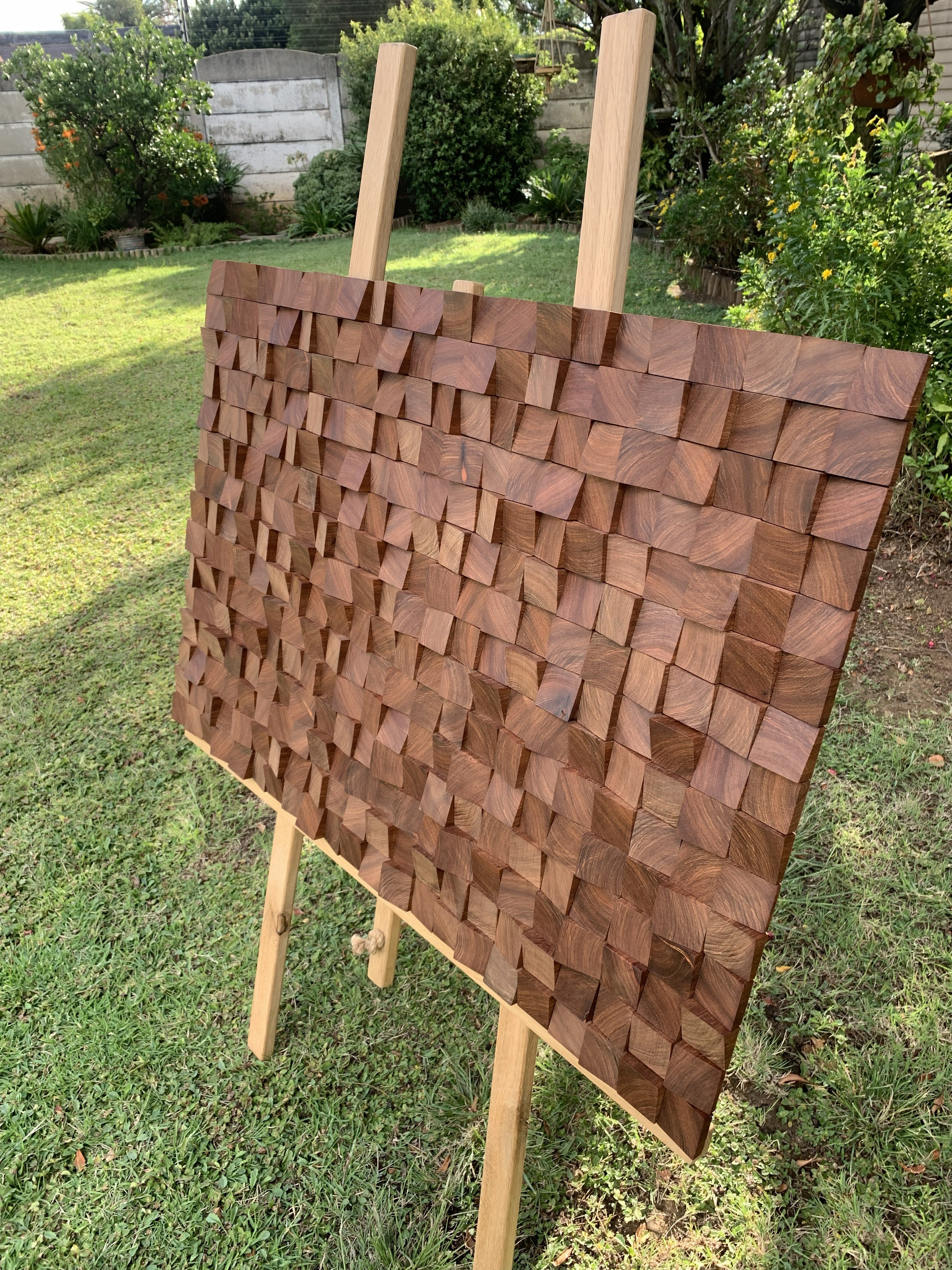 Commissioned Kiaat wooden block wall art displayed on an easel outdoors, showing the angled block texture and natural wood grain.