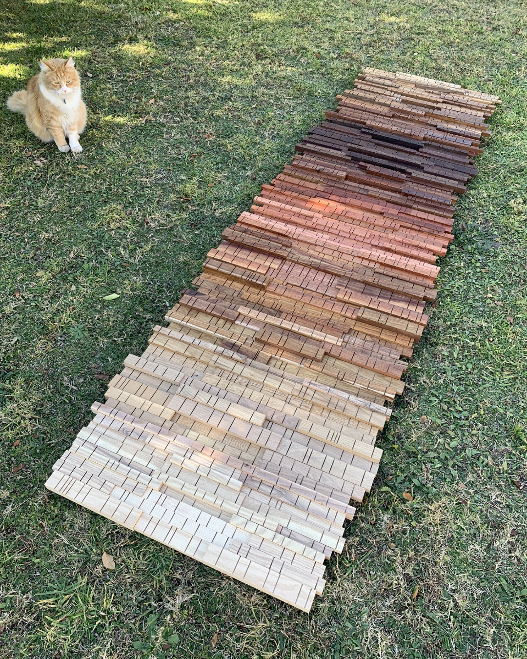Large handcrafted wooden wall artwork laid out before installation, showing the natural gradient of mixed hardwood species.